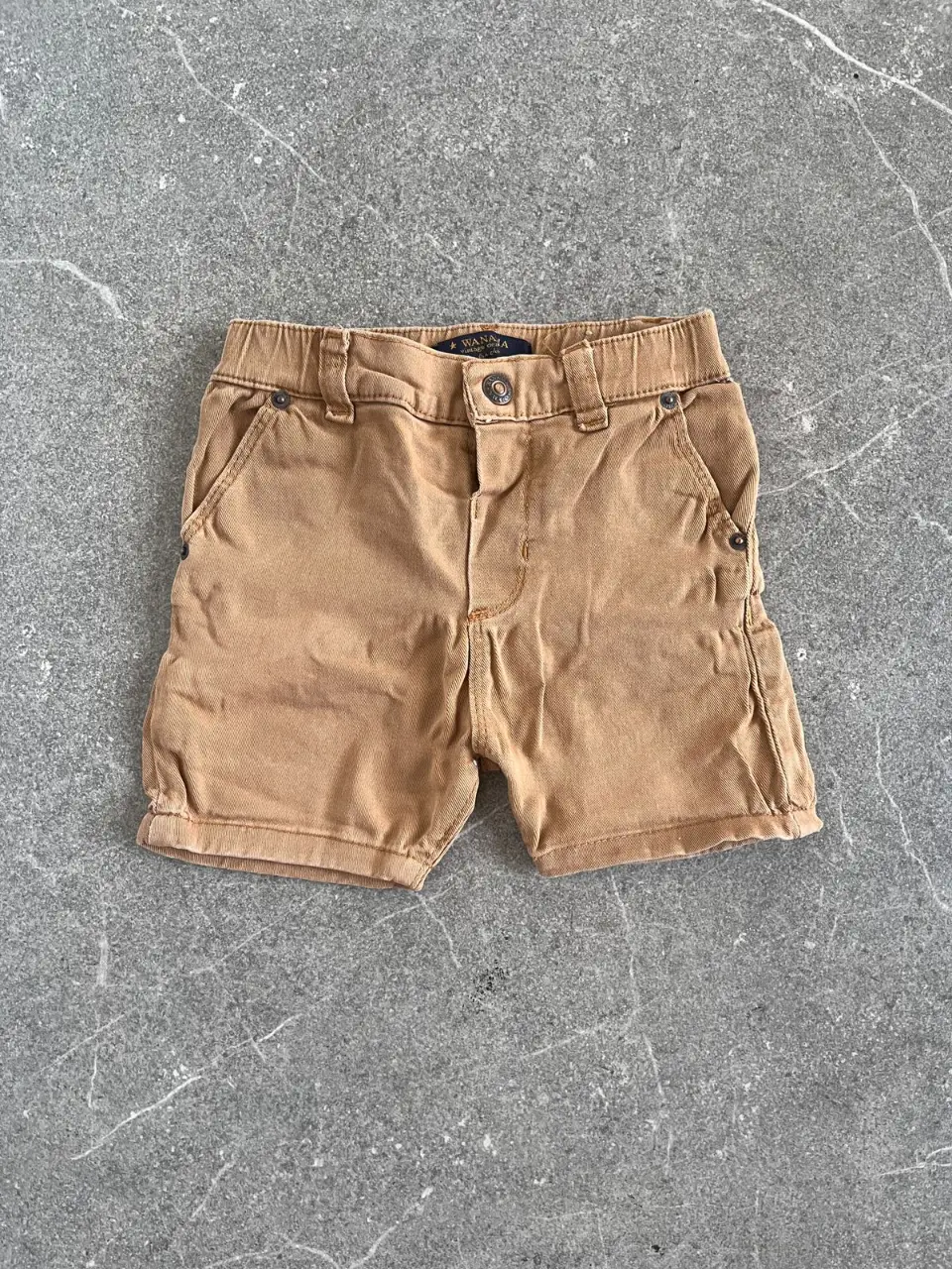Short de niño color marrón claro, con bolsillos y detalles de la marca Wanama en la parte trasera. Ideal para un look casual y cómodo.