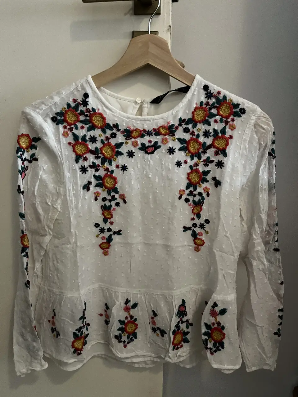 Blusa blanca de Zara con bordado floral multicolor. Cuello redondo y manga larga. Ideal para un look casual y femenino.