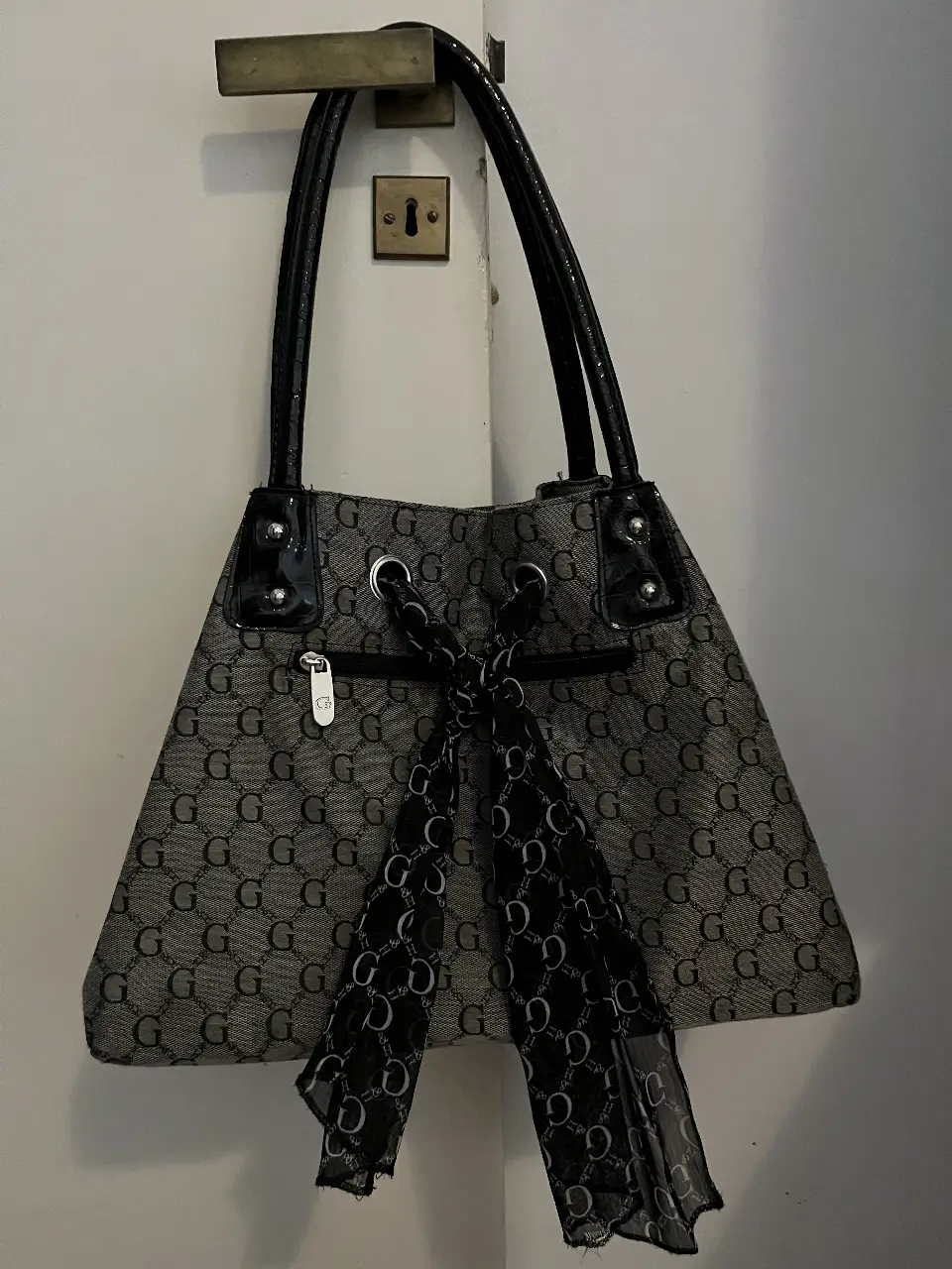 Cartera Guess gris con estampado de la marca y detalles en negro. Ideal para llevar al hombro.
