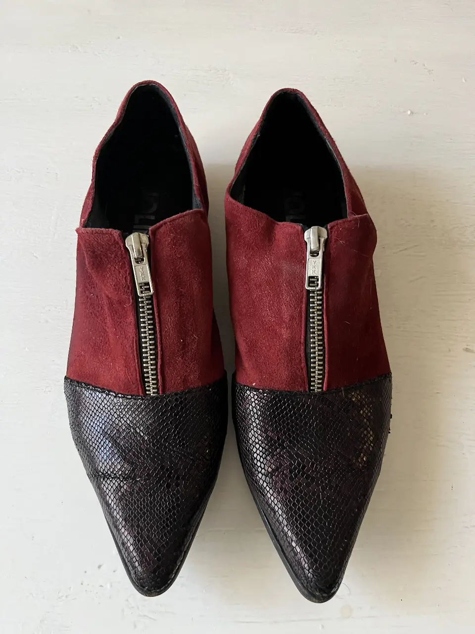 Botines de mujer con puntera de cuero símil reptil y capellada de gamuza roja. Cierre frontal plateado. Ideales para un look moderno y sofisticado.