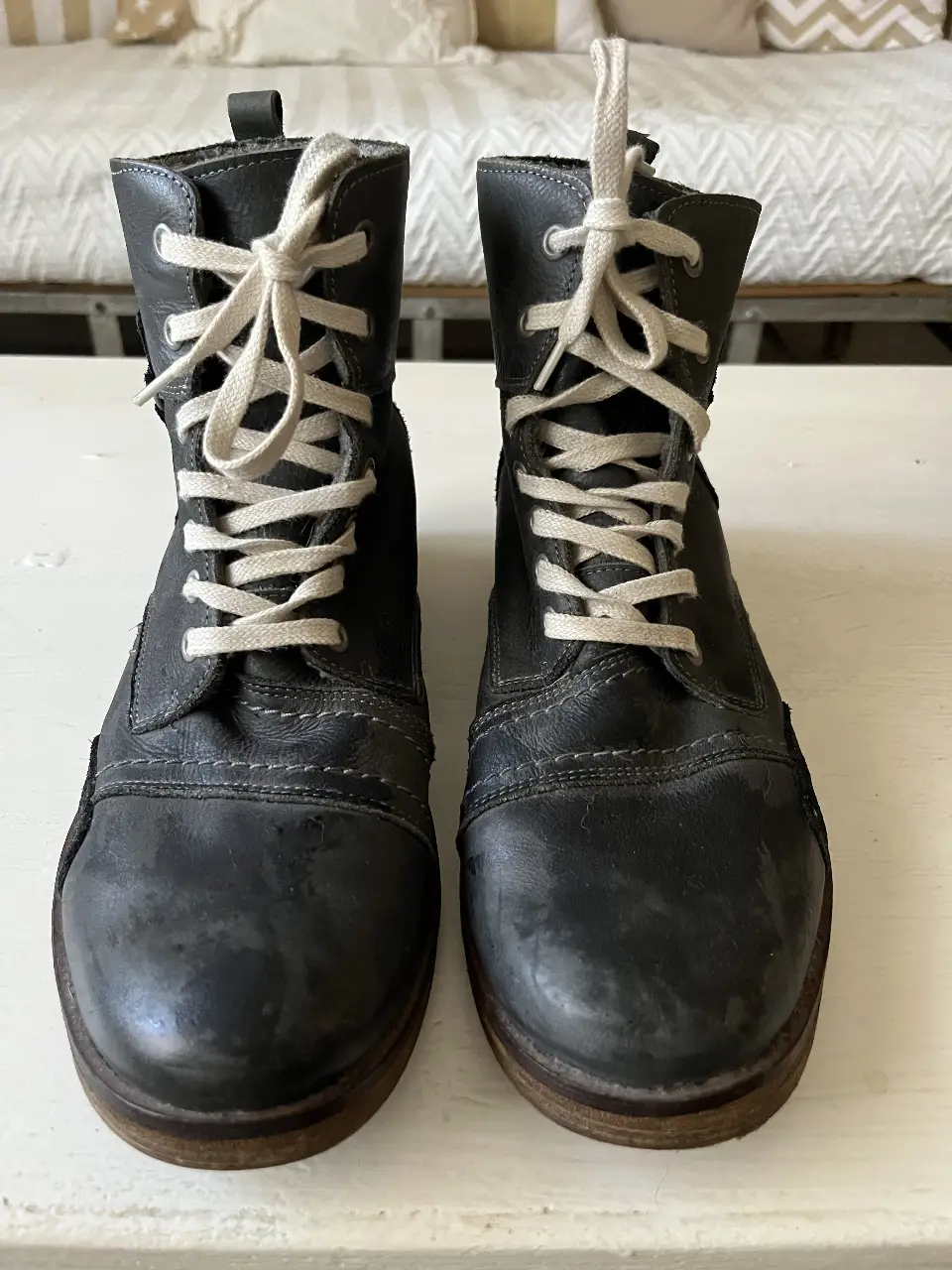 Botines de cuero gris oscuro con cordones beige. Tienen un estilo vintage y detalles de costura. Ideales para un look casual y urbano.