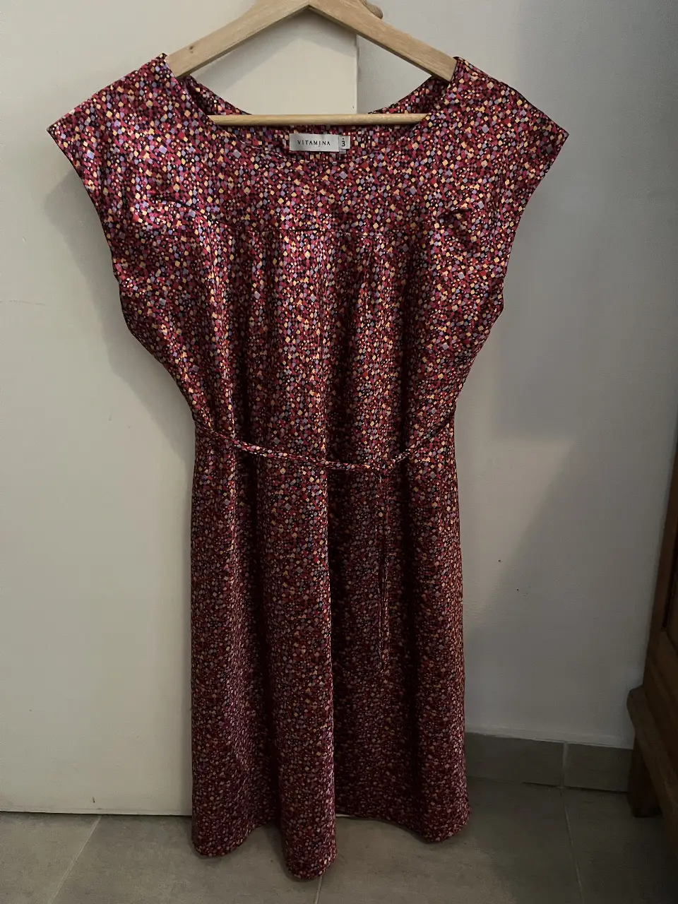 Vestido midi de la marca Vitamina, con estampado floral en tonos borgoña, rosa y amarillo. Tiene mangas cortas y un cinturón para ajustar la cintura. Ideal para un look elegante y femenino.