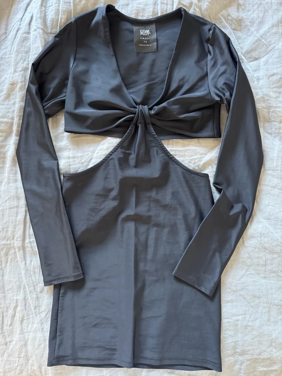 Vestido negro con escote anudado y mangas largas. Posee recortes en la zona del abdomen y falda corta.