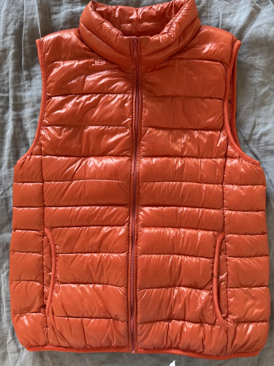 Chaleco acolchado naranja con cuello alto y cierre completo. Posee bolsillos laterales.