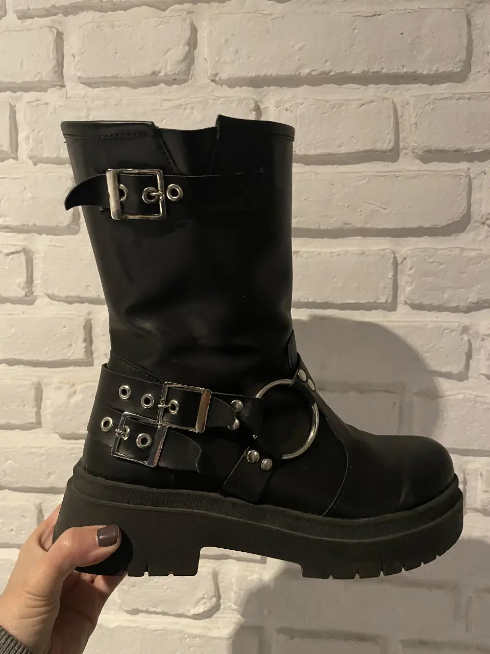 Botas negras de caña alta con detalles de hebillas y argollas metálicas. Plataforma gruesa para un look audaz y moderno. Ideales para un estilo rocker o urbano.