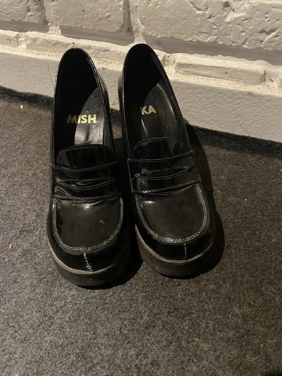 Zapatos de taco alto negros con plataforma y estilo mocasín. Tienen detalles de charol y la marca MISH KA en la plantilla. Ideales para un look elegante y moderno.