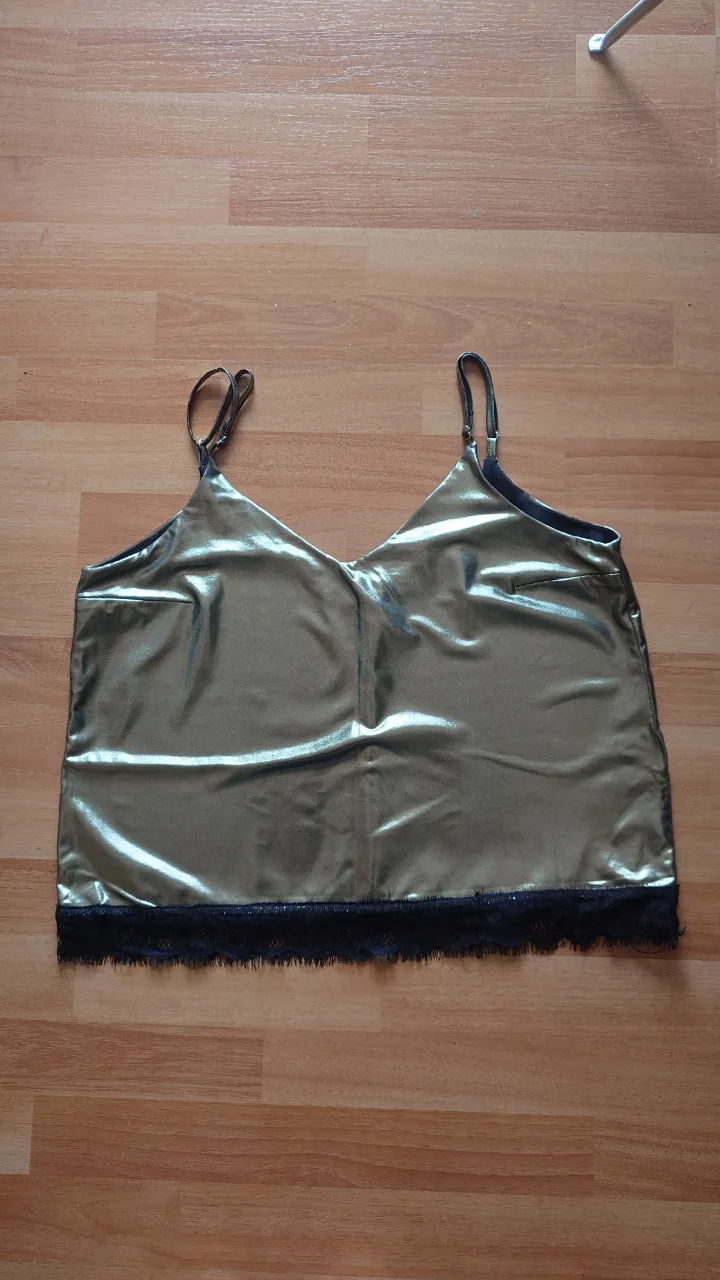 Top de mujer con tirantes finos y escote en V. Diseño metalizado dorado con detalle de encaje negro en el bajo. Ideal para fiestas o salidas.