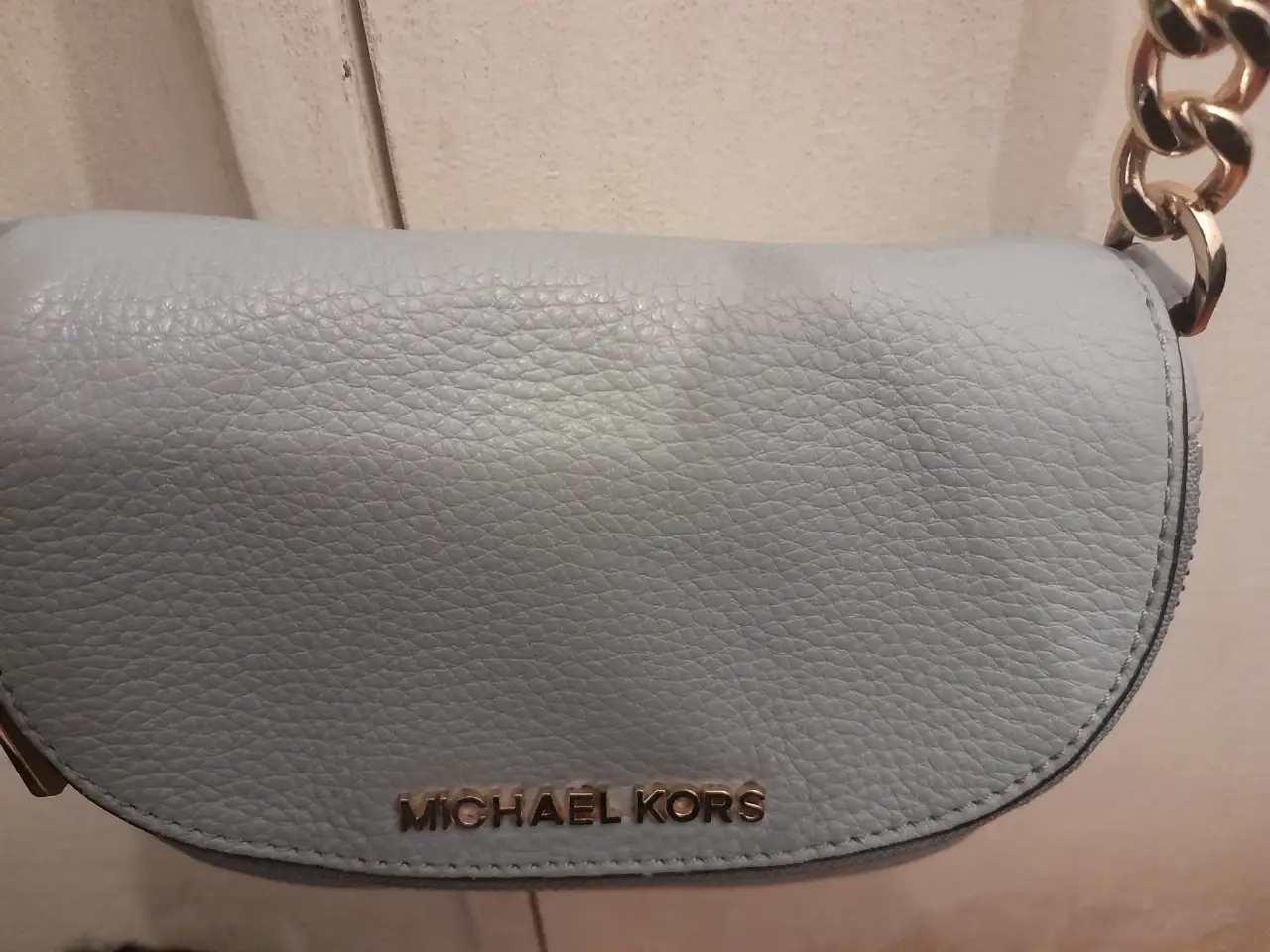 Cartera bandolera Michael Kors de cuero celeste, con cadena dorada y cierre. Ideal para un look casual y elegante.