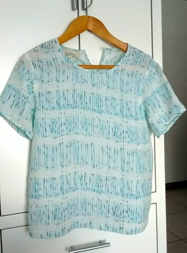 Blusa de mujer con estampado de líneas verticales en tonos celeste y blanco. Cuello redondo y mangas cortas. Ideal para un look fresco y casual.