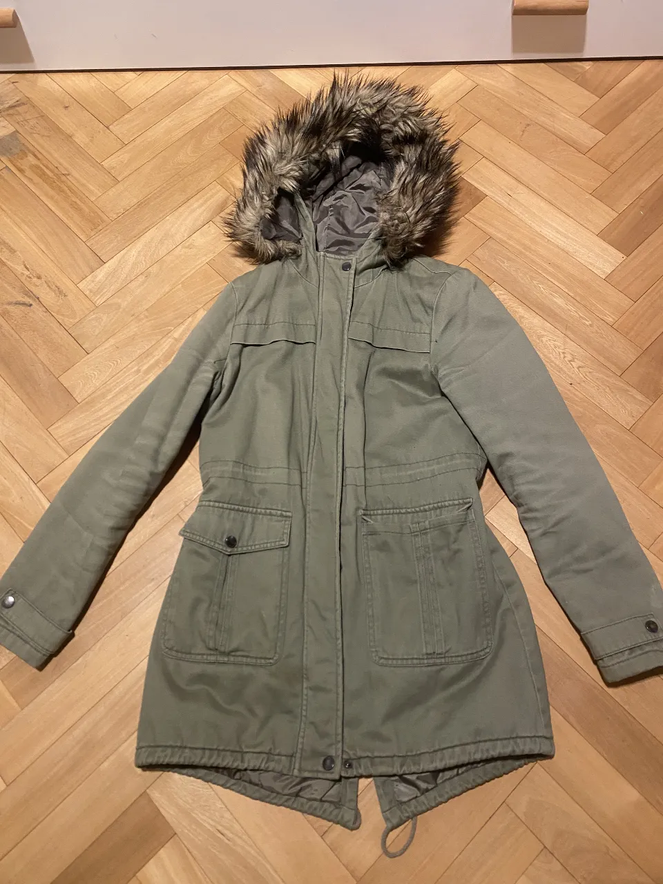 Campera parka verde militar con capucha de piel sintética, ideal para el invierno. Cuenta con bolsillos delanteros y ajuste en la cintura. Talle S, de la marca Sybilla.