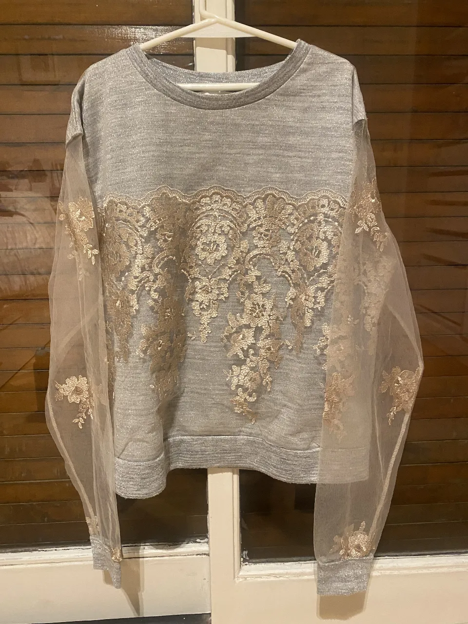 Buzo de mujer gris con detalles dorados de encaje en el frente y mangas de tul. Ideal para un look elegante y sofisticado. Casi sin uso.