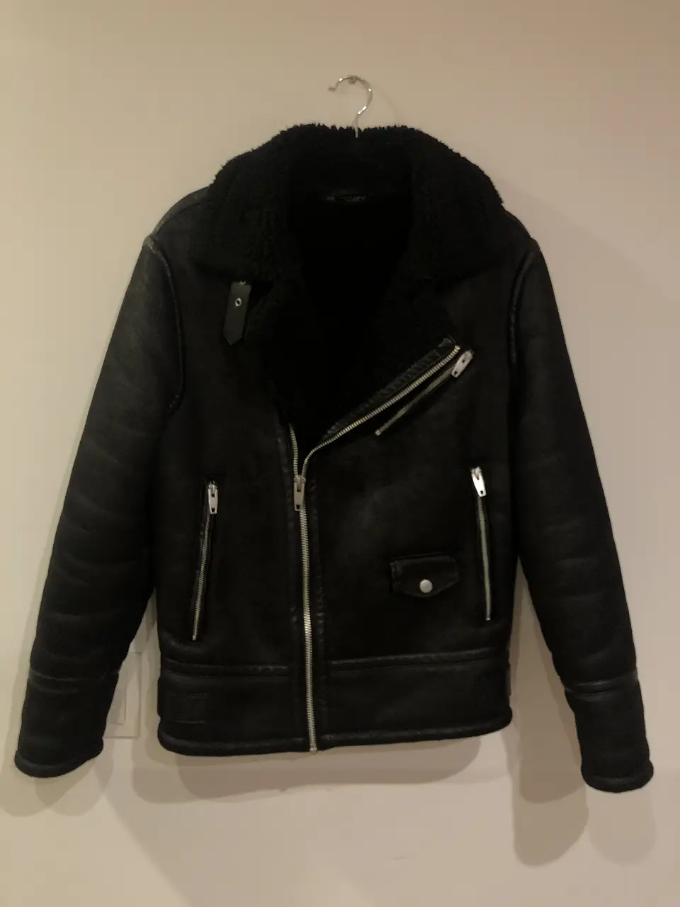 Campera biker de cuero sintético negra de Zara, con cuello con solapas y forro de borreguito. Posee cierre y bolsillos con cremallera. Talle M.