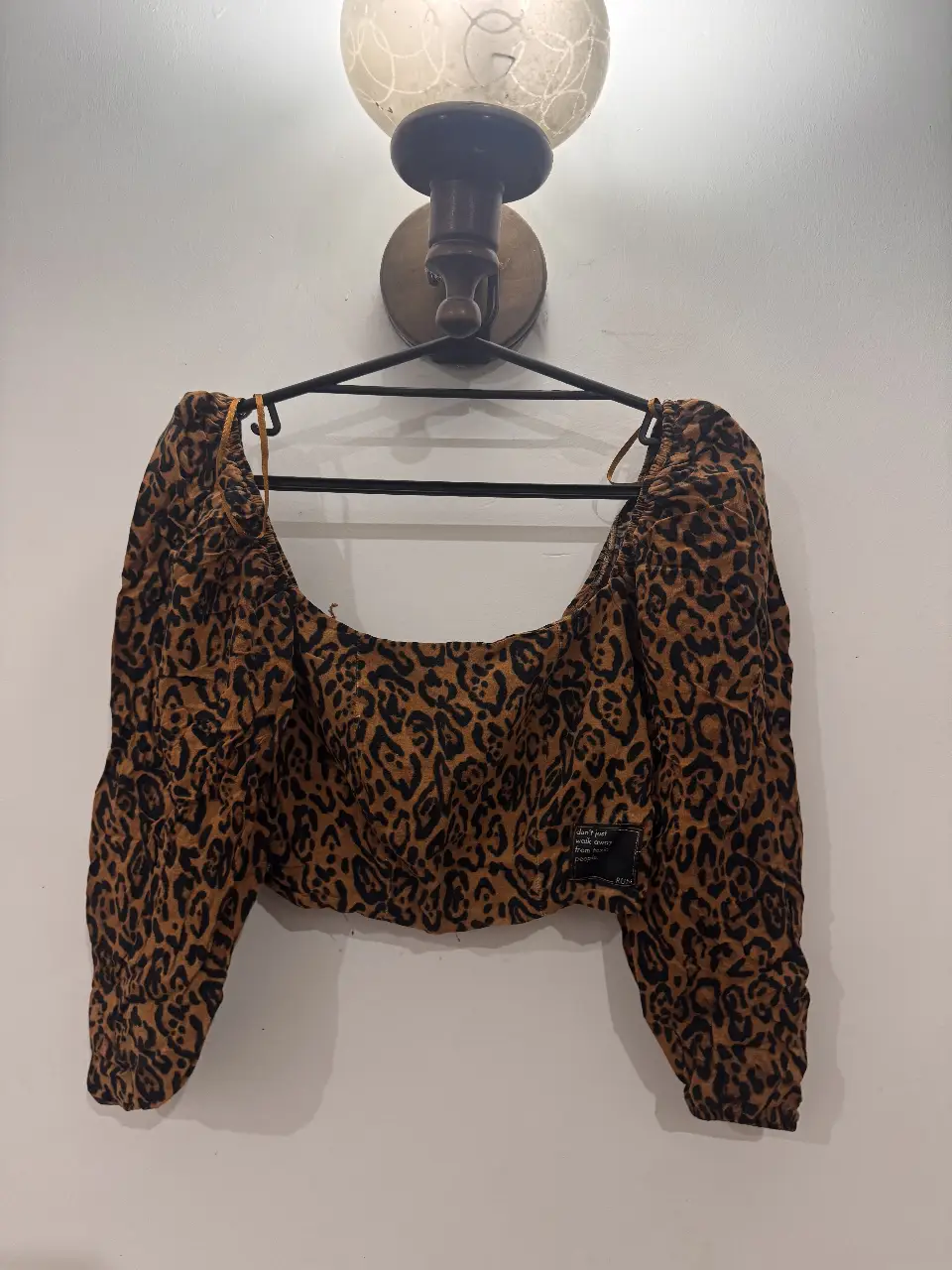 Top corto con estampado de leopardo. Tiene mangas 3/4 abullonadas y un detalle de etiqueta con frase. Ideal para un look moderno y audaz.