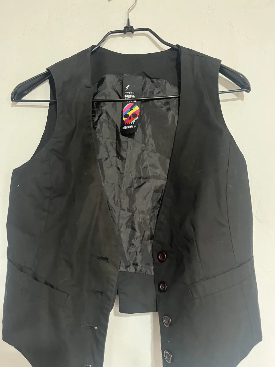 Chaleco negro de vestir, ideal para complementar outfits formales o darle un toque chic a looks más casuales. Posee botones al frente y un detalle de hebilla ajustable en la espalda para un mejor calce.