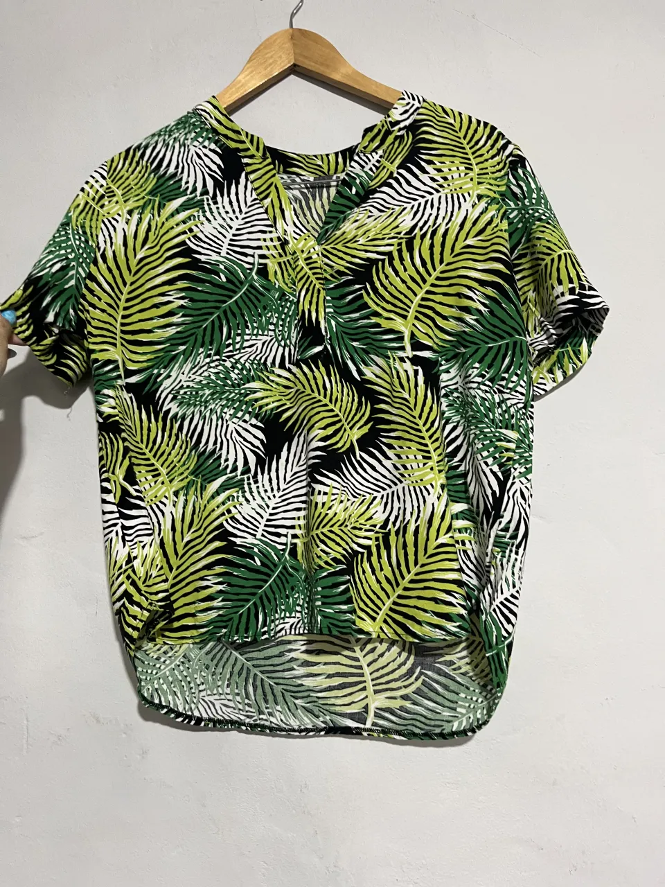 Remera estampada con hojas tropicales en verde y blanco sobre fondo negro. Diseño fresco y moderno, ideal para un look casual y relajado.