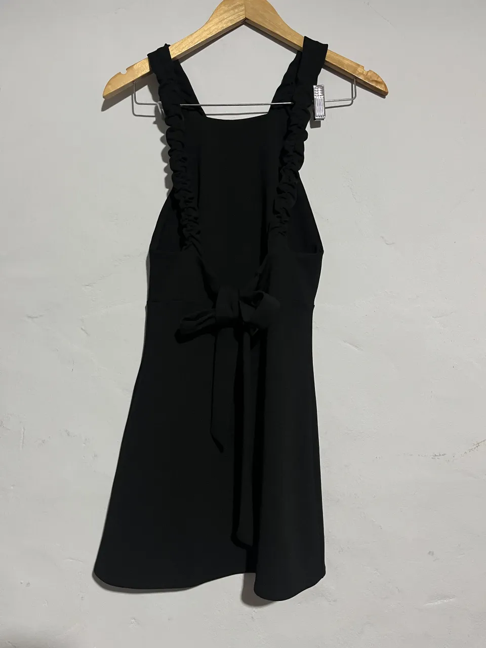 Vestido negro corto con tiras finas y detalle de volados en los hombros. Espalda descubierta con lazo para atar.