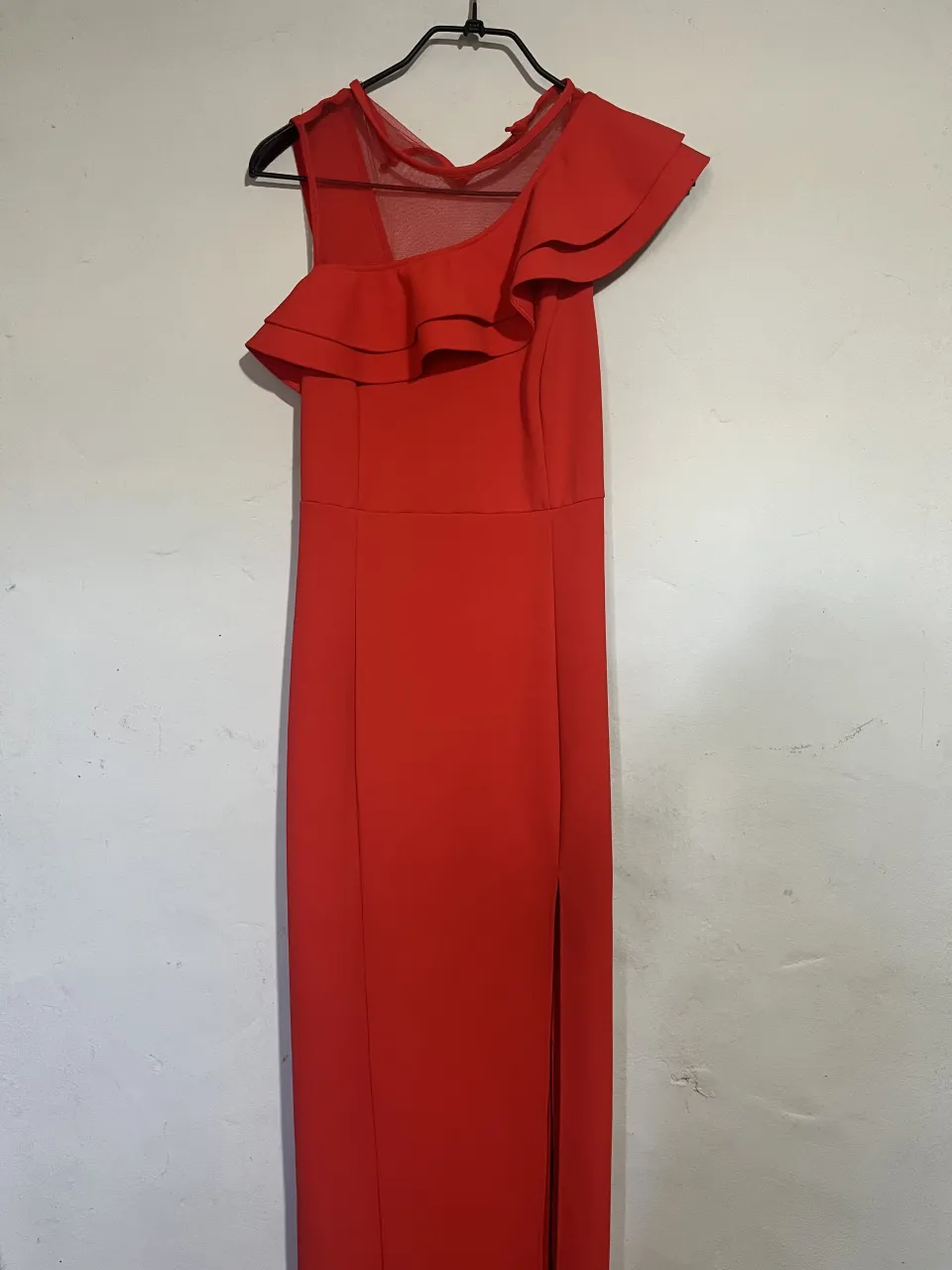 Vestido largo rojo, con un diseño asimétrico en el hombro con volados y detalles de tul en el escote. Posee una abertura lateral en la falda. Ideal para eventos formales o fiestas.