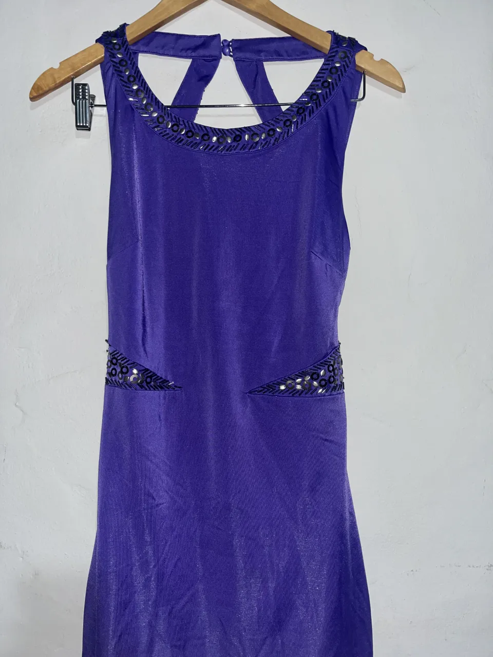 Vestido largo de fiesta, color violeta intenso, con detalles de pedrería plateada en cuello y cintura. Espalda descubierta con tiras cruzadas y cierre en la parte inferior. Ideal para eventos formales y celebraciones.