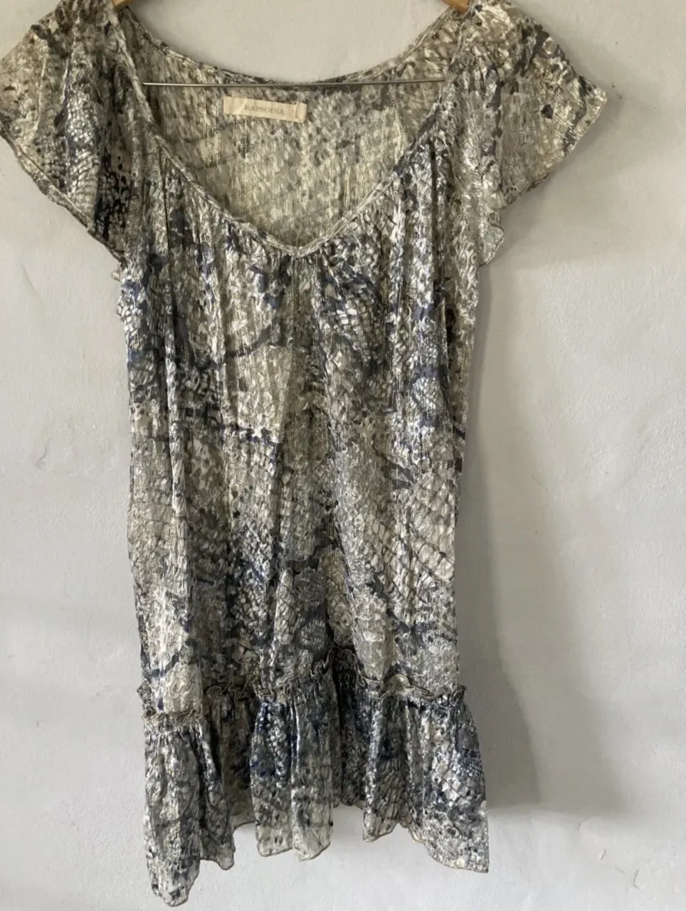 Vestido corto con estampado abstracto en tonos grises y azules. Posee volados en la parte inferior y mangas cortas. Ideal para un look casual y canchero.(VIENE CON UNA TIRA PARA ATAR EL VESTIDO) 