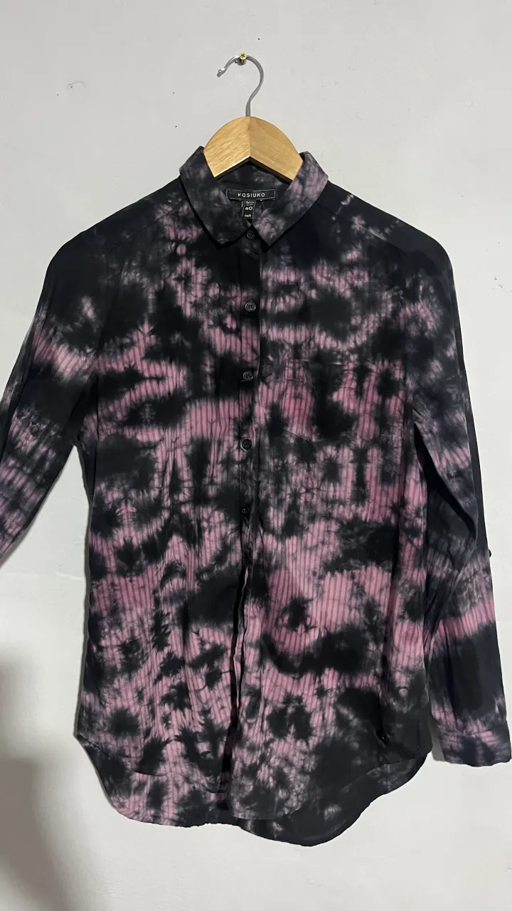 Camisa de manga larga con estampa tie-dye en tonos negros y rosas. Un diseño moderno y canchero, ideal para darle un toque original a tu look. Perfecta para combinar con jeans o pantalones de cuero.