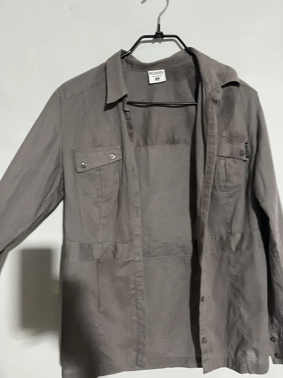 Camisa de manga larga gris, ideal para un look casual o de trabajo. Confeccionada en un tejido liviano, presenta bolsillos con solapa en el pecho y detalles de costuras que le dan un toque moderno. Perfecta para combinar con jeans o pantalones de vestir.