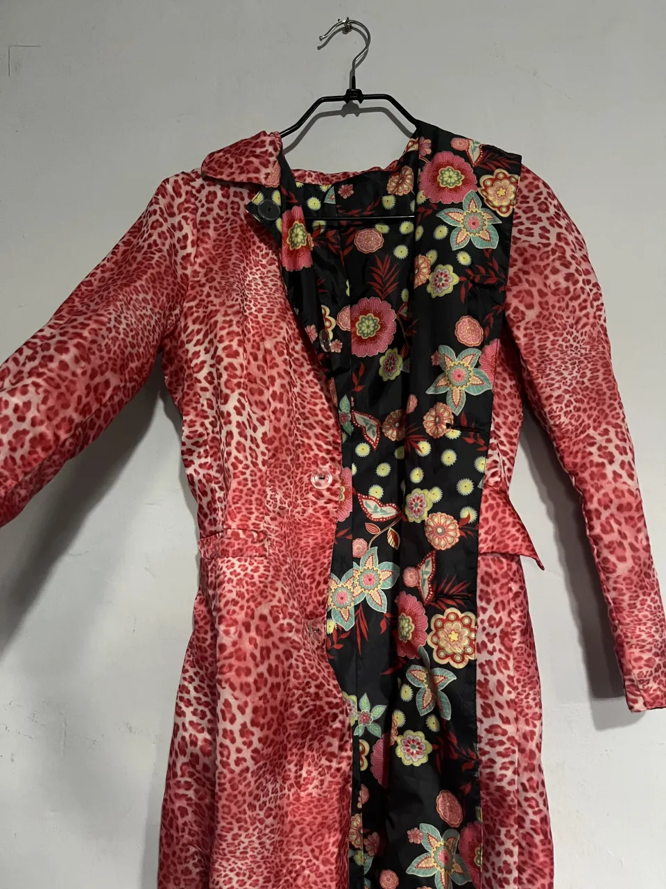 Abrigo largo reversible con estampado de leopardo en rosa y negro por un lado, y un estampado floral vibrante sobre fondo negro por el otro. Diseño único con solapa y cinturón para anudar. Ideal para darle un toque audaz y chic a tu look.