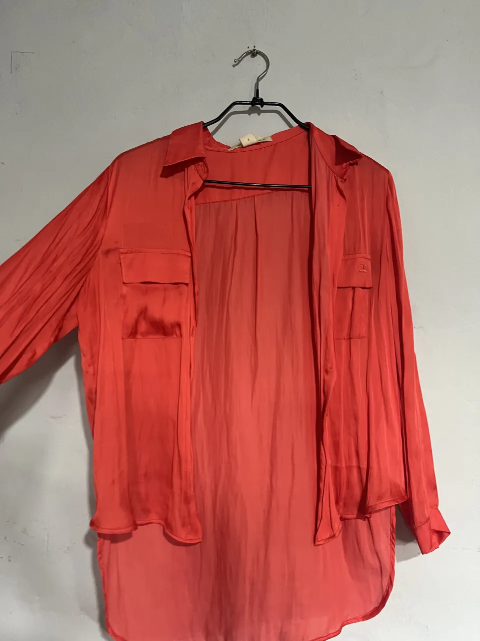 Camisa de seda color coral, con bolsillos en el frente y mangas largas. Ideal para un look elegante y casual.