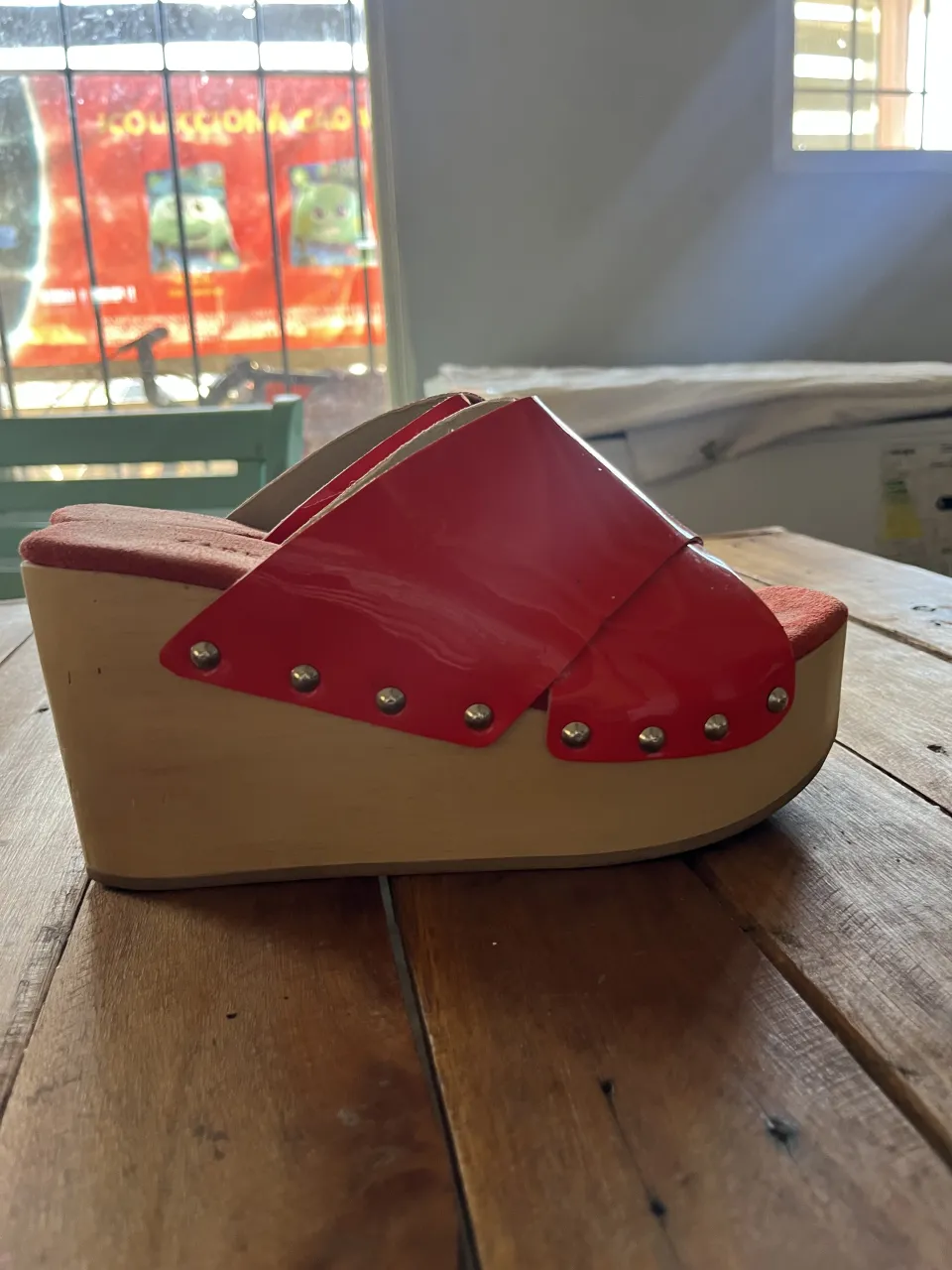 Sandalias de plataforma rojas con tiras anchas y tachas metálicas. La base es de madera.