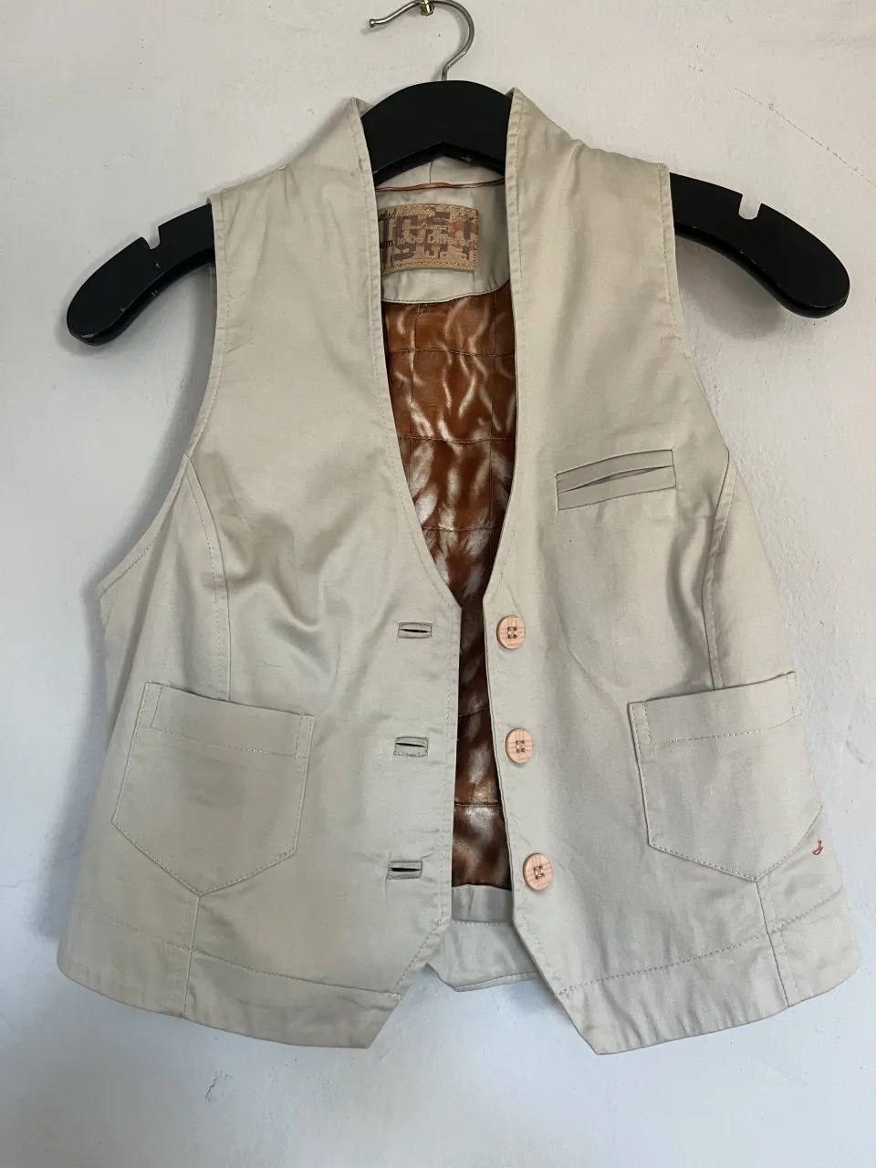 Chaleco de gabardina color crudo, con forro interno estampado en tonos marrones y blancos. Posee botones a tono y bolsillos frontales. Ideal para un look casual y canchero.