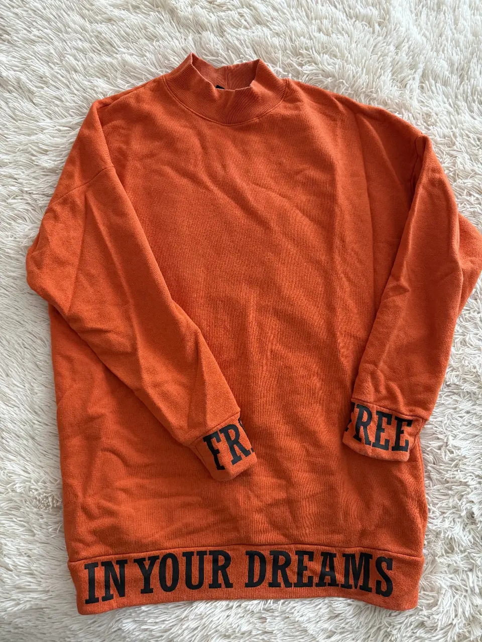 Buzo naranja con cuello alto y puños con la palabra "FREE" y "IN YOUR DREAMS" en la parte inferior. Ideal para un look casual y cómodo.