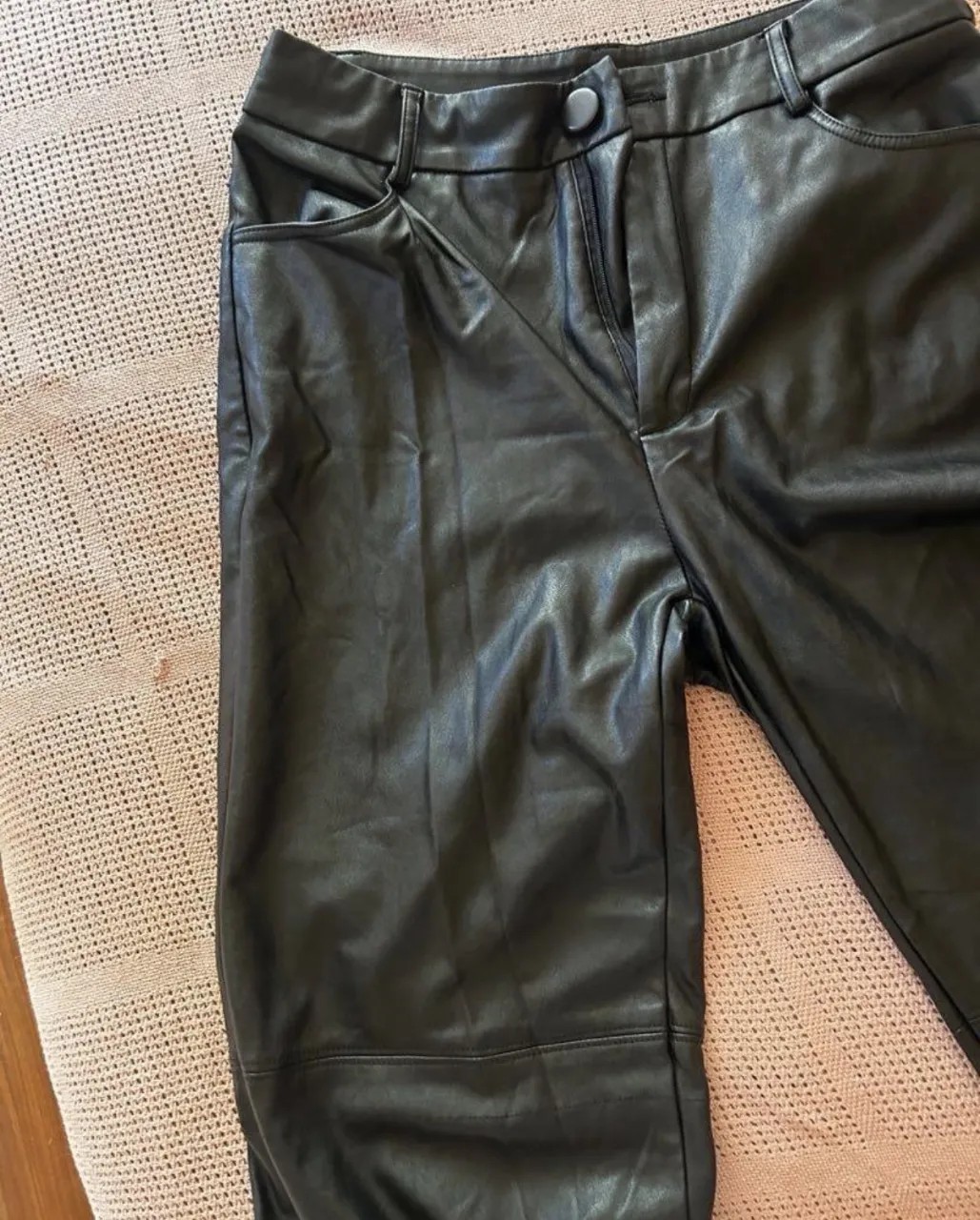 Pantalón de cuero sintetico negro con cierre y un botón en la cintura. Posee bolsillos delanteros.