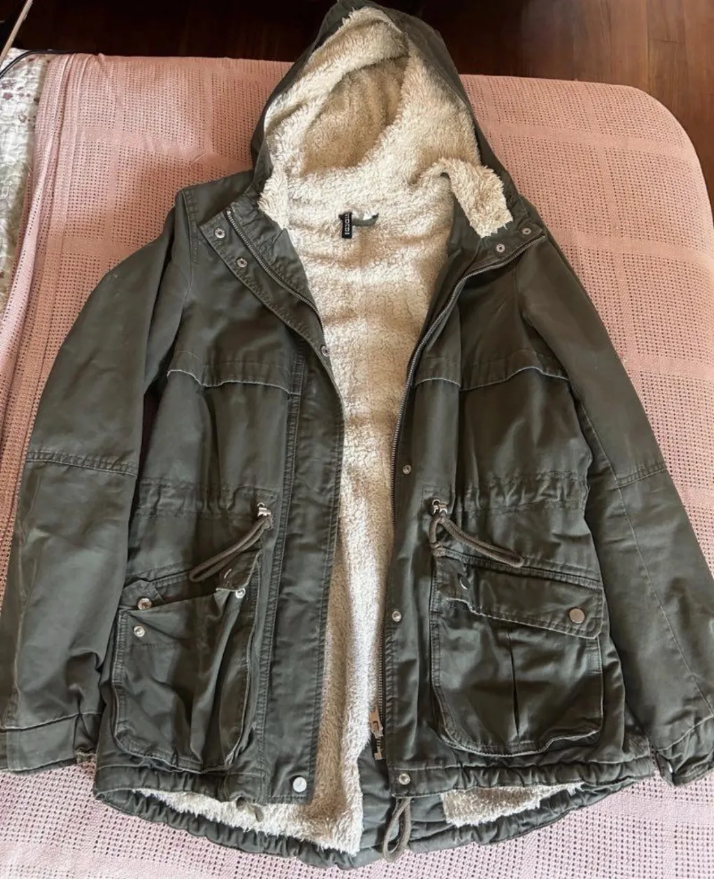 Campera verde con capucha forrada en corderito. Posee bolsillos frontales con solapa y cordones ajustables en la cintura y en el ruedo.