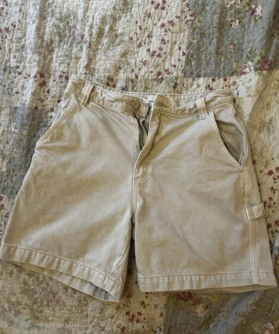 Shorts de gabardina color tiza. Cuentan con bolsillos delanteros y traseros, y un pequeño bolsillo adicional en el lateral derecho. Cierre de botón y cierre.