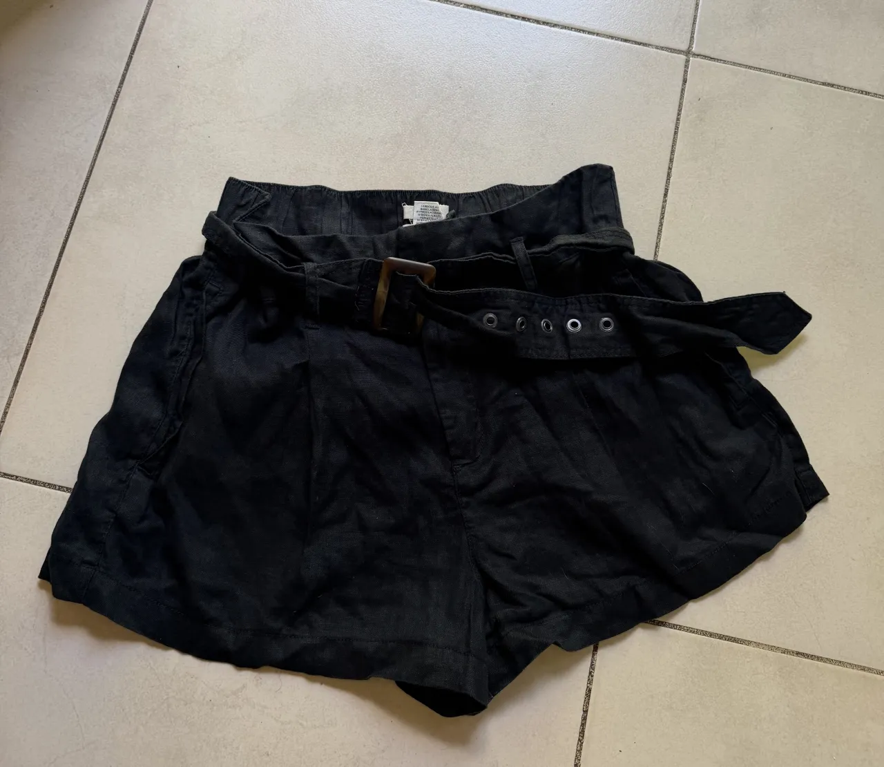 Shorts de Lino con cinturón y hebilla de madera. Cintura con elástico y presillas para el cinturón. Posee bolsillos laterales.