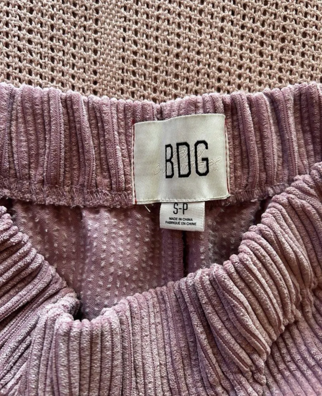 Pantalón de pana color rosa pálido con cintura elastizada. Posee pinzas delanteras y botamangas anchas.