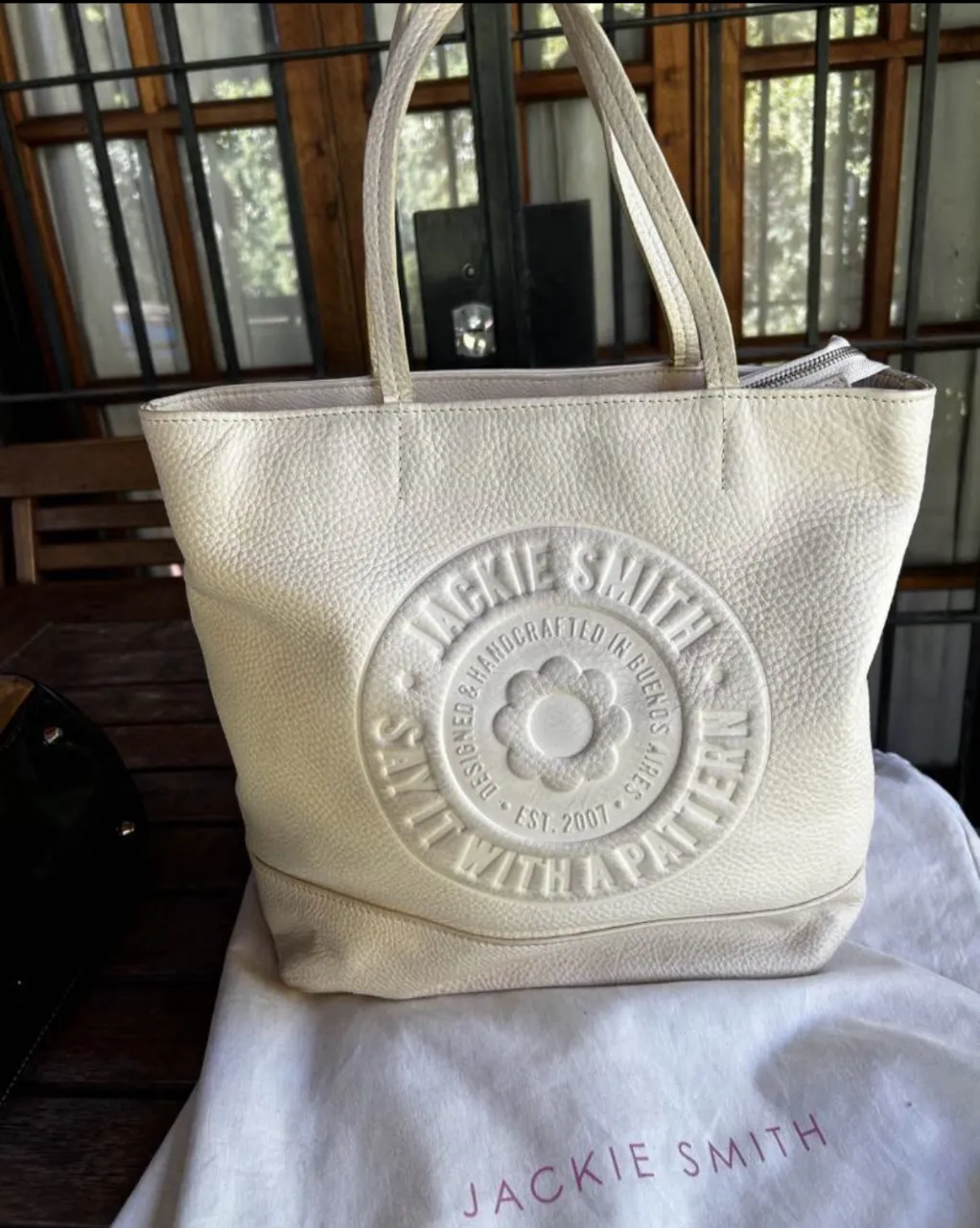 Bolso de Jackie Smith de cuero color crudo con logo circular en relieve en el frente. Interior forrado a rayas.