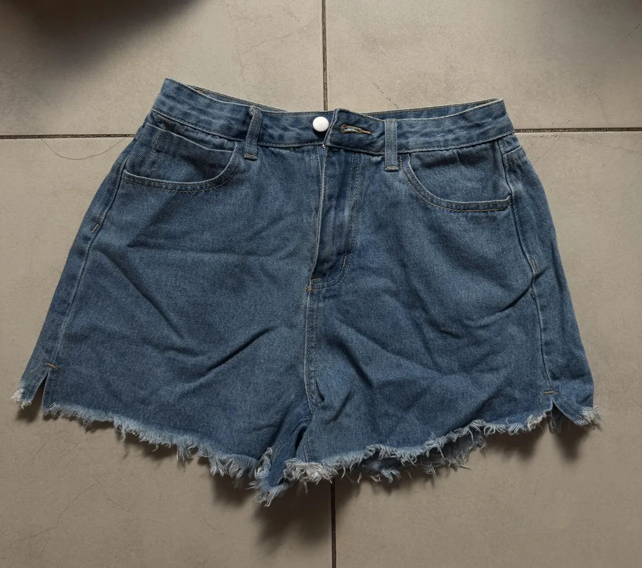 Shorts de jean tiro alto con roturas y flecos en el ruedo. Posee bolsillos delanteros y traseros.