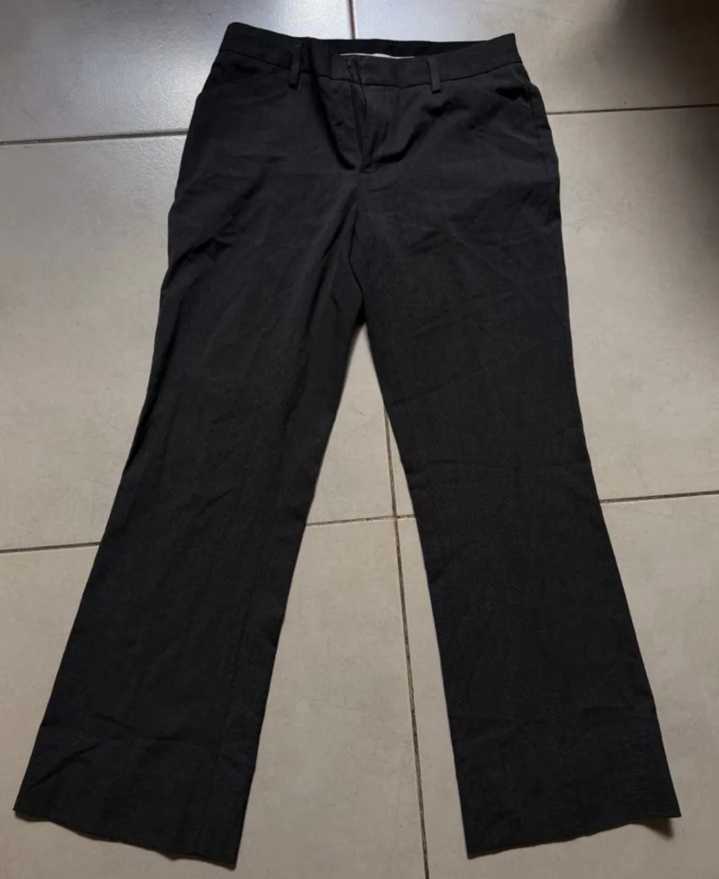 Pantalón de vestir gris con finas rayas verticales. Posee bolsillos frontales y presillas para cinturón.