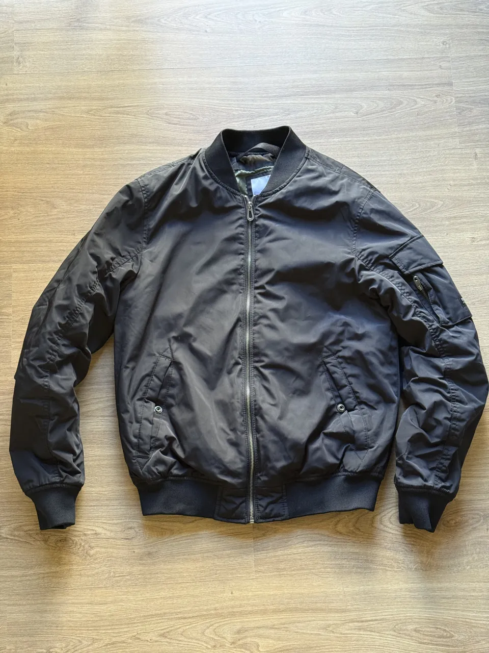 Campera bomber negra con cierre al frente, bolsillos laterales y en manga izquierda. Puños y cuello de ribb.