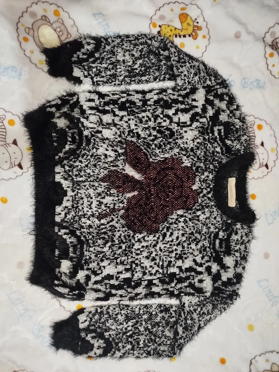 Sweater de tejido grueso con estampa abstracta en blanco y negro. Posee un detalle de flor bordada en el frente en tono marrón. Ideal para un look canchero y abrigado.