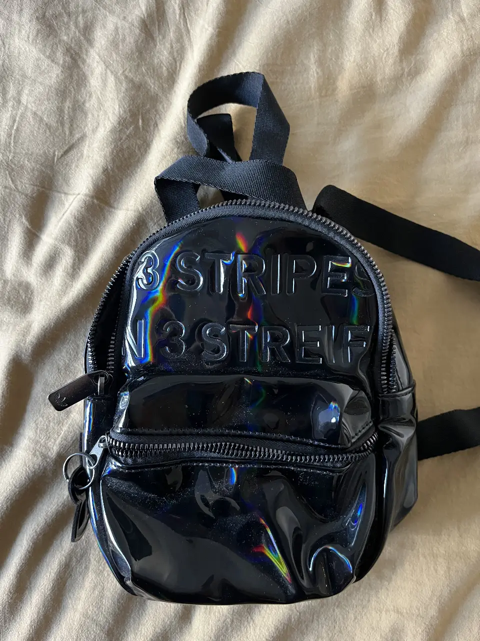 Mochila Adidas Mini 3 Stripes, negra con efecto holográfico. Ideal para llevar lo esencial con estilo.