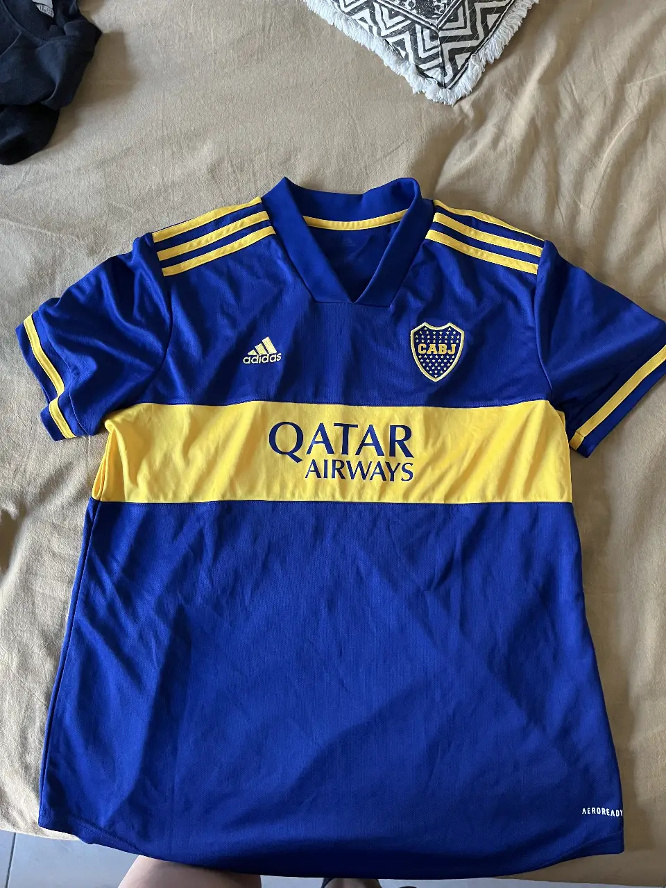 Camiseta de fútbol de Boca Juniors, azul con franja amarilla y detalles de Adidas y Qatar Airways. Ideal para fanáticos y coleccionistas.