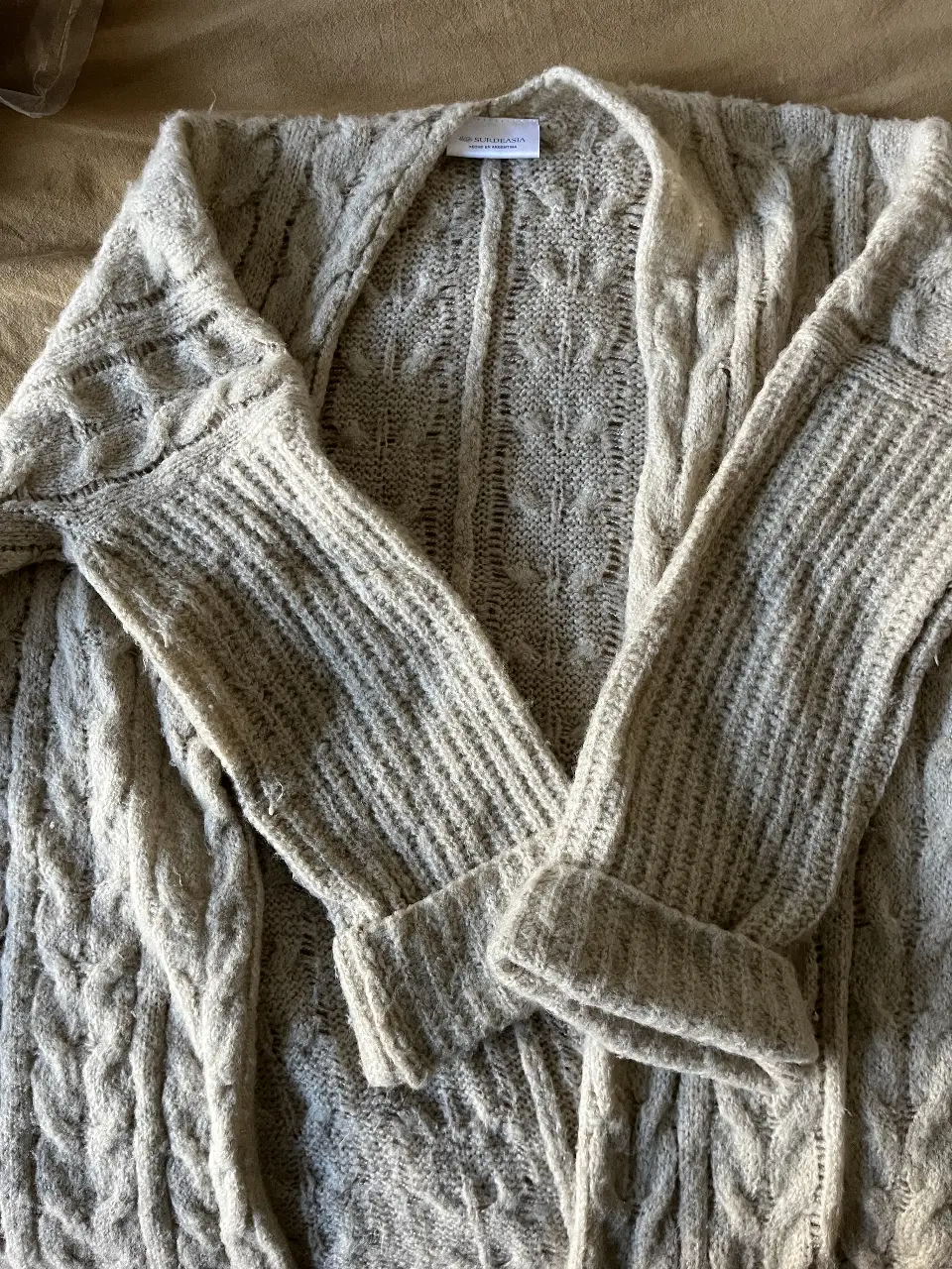 Cardigan tejido de lana color beige , con diseño de trenzas y cuello abierto. Ideal para un look casual y abrigado.