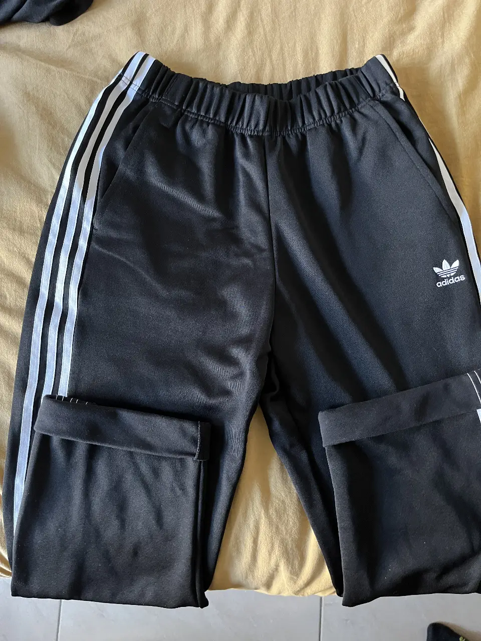 Pantalón deportivo Adidas negro con las clásicas tres tiras blancas a los costados. Confeccionado con material Primeblue, hecho con plástico reciclado del océano. Ideal para un look casual y cómodo.