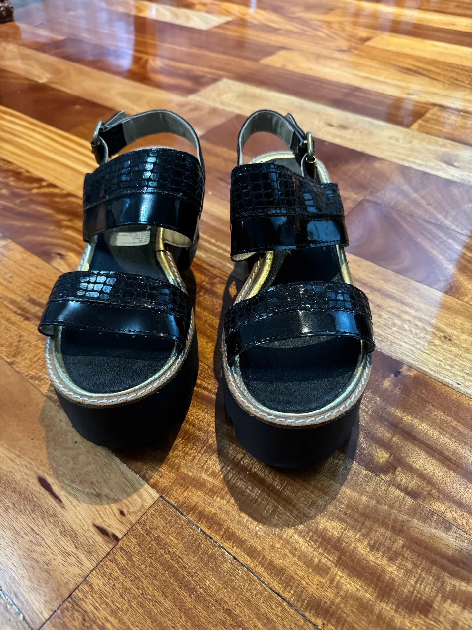 Sandalias negras con plataforma y detalles de charol. Ideales para un look moderno y cómodo.