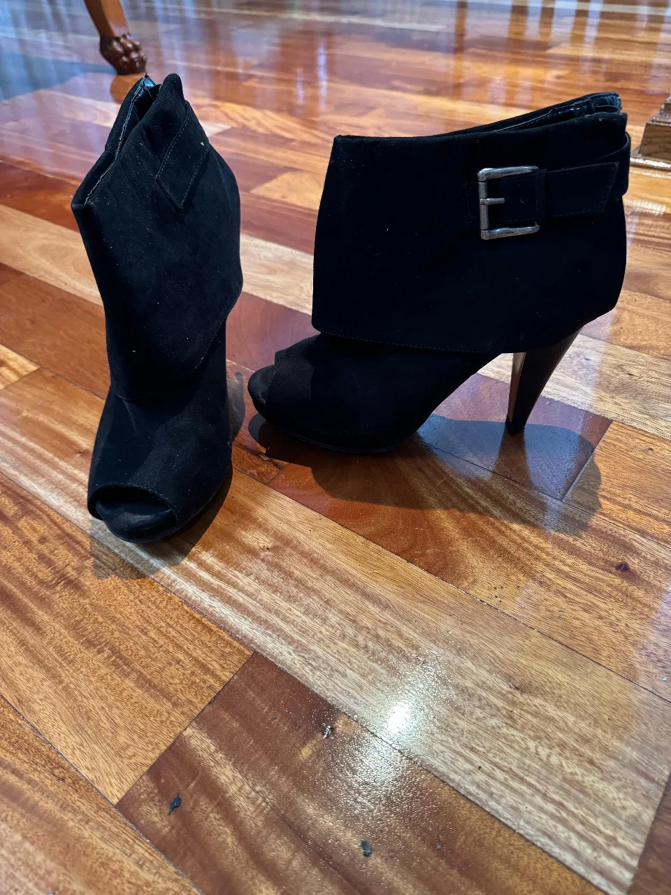 Botines negros de gamuza con taco alto y diseño peep toe. Detalles de hebilla y solapa.