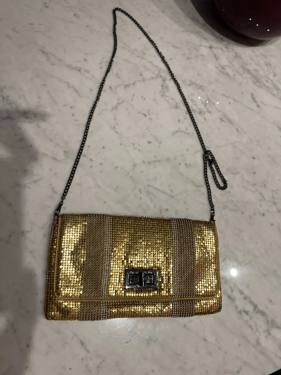 Cartera dorada de mano con cadena para colgar. Ideal para eventos y fiestas. Marca BCBG maxmaria. En el interior, a la altura del cierre tiene una mancha.