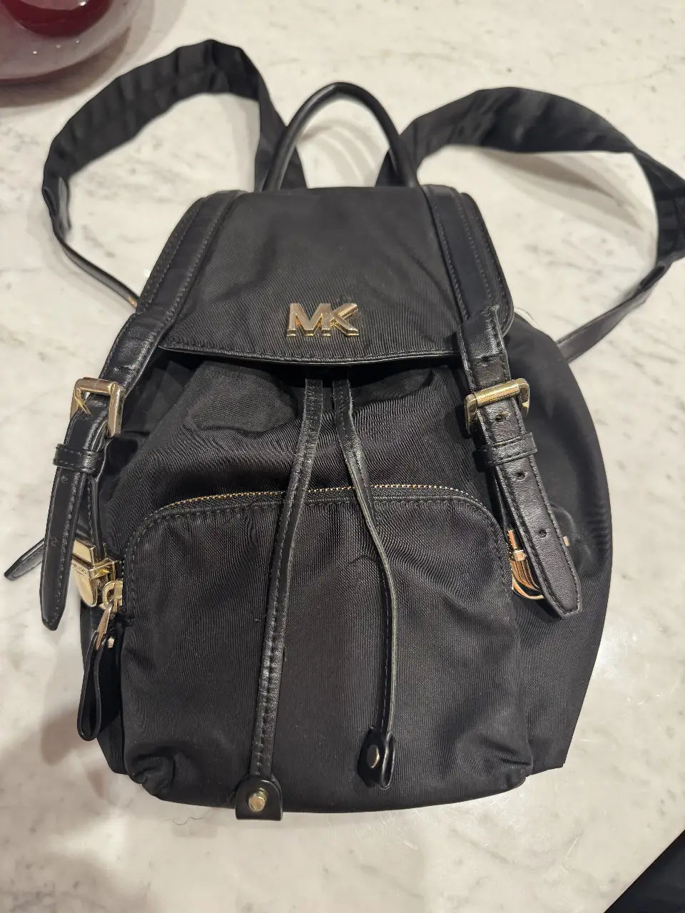Mochila negra Michael Kors, ideal para uso diario. Confeccionada en material resistente, cuenta con un bolsillo frontal con cierre y detalles dorados. Perfecta para llevar tus esenciales con estilo.