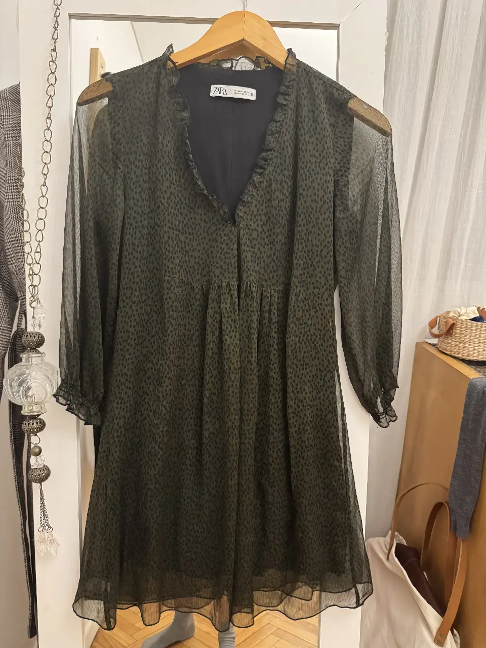 Vestido midi de gasa con estampado de lunares en verde oscuro. Cuello en V con volados, mangas largas con puños y corte en la cintura. Ideal para un look elegante y versátil.