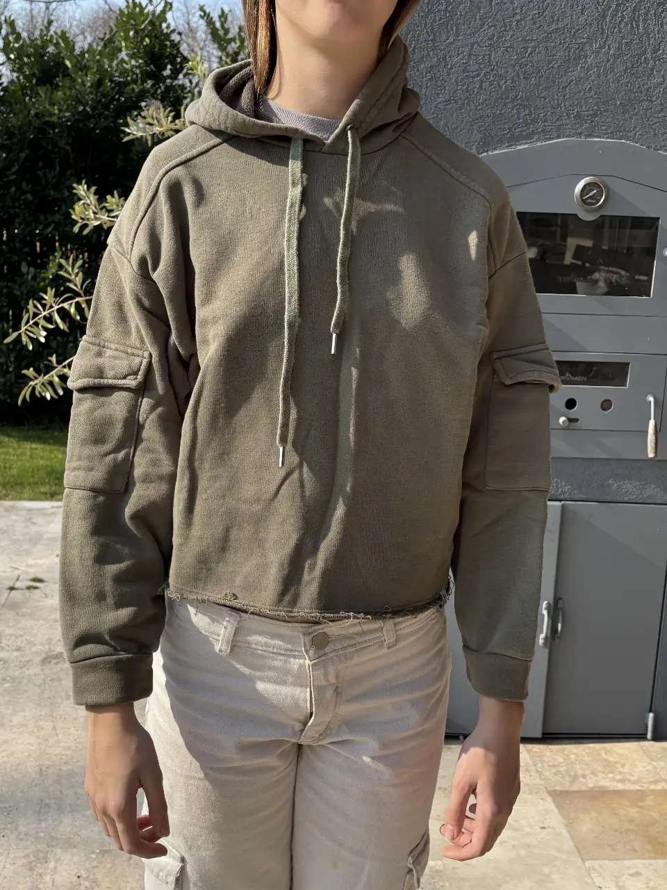 Buzo canguro de mujer, color verde militar, con capucha y bolsillos tipo cargo en las mangas. Corte cropped con terminación desflecada. Ideal para un look casual y canchero.